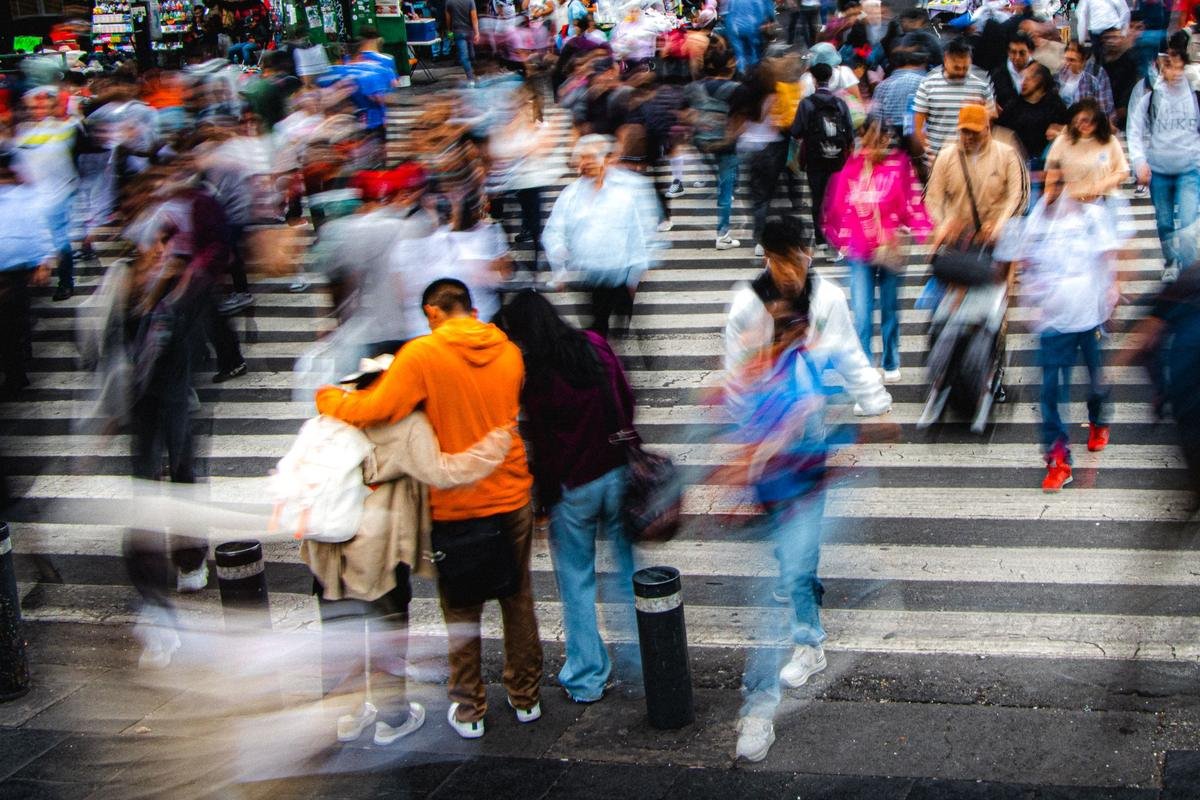 Multitud cruzando una calle en hora pico, con las figuras movidas por el tiempo de exposición