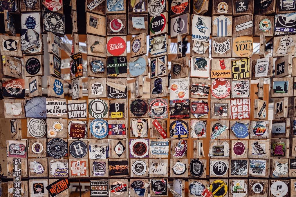 Muro cubierto de cientos de calcomanías con logotipos y emblemas distintos, cada uno en su propia placa de madera