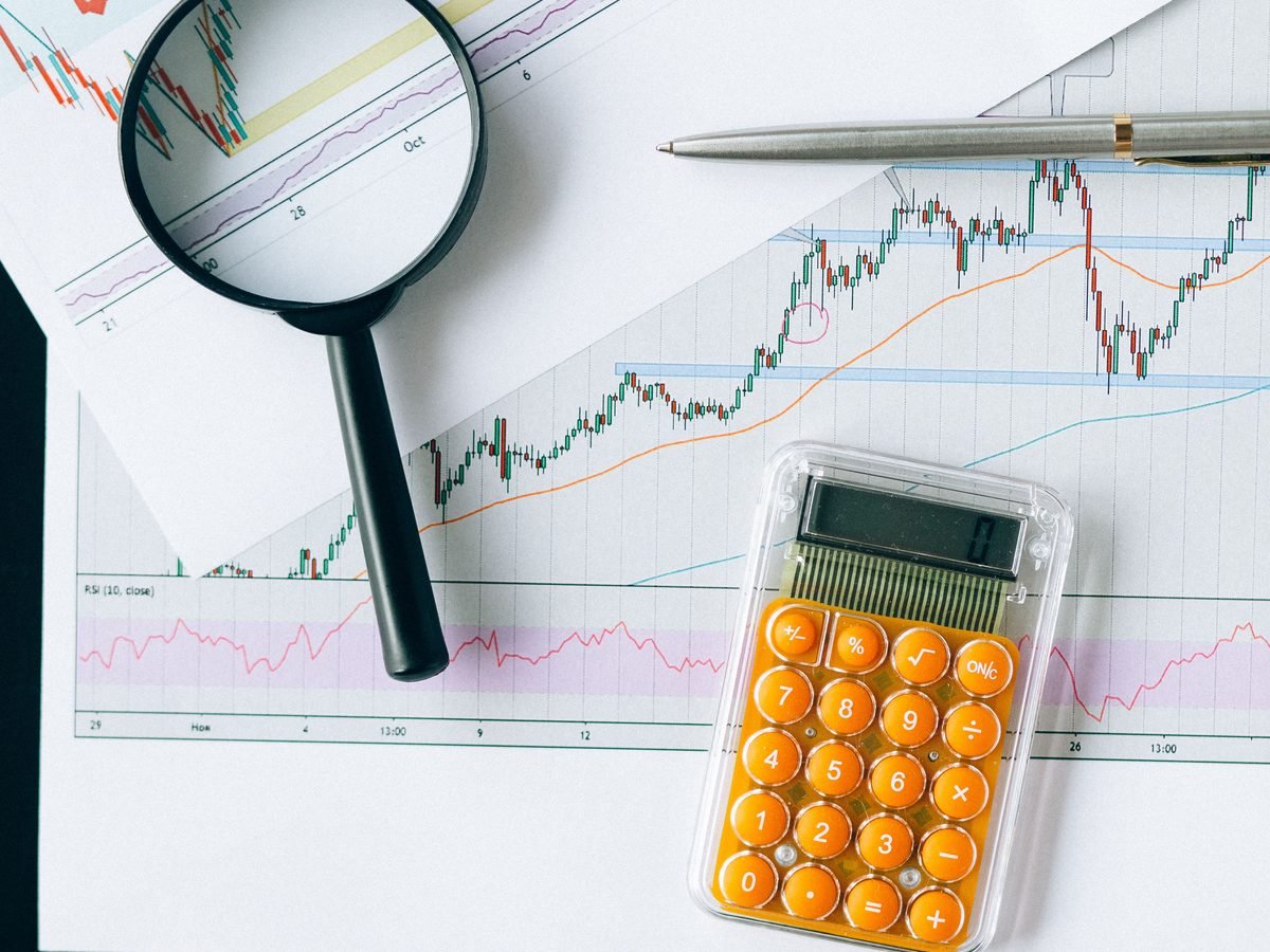 Una lupa sobre una gráfica de líneas ascendente, junto a una calculadora y un bolígrafo